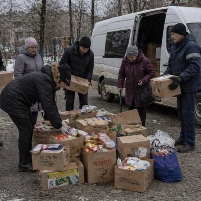 People organizing boxes of food and household supplies beside a delivery van in winter