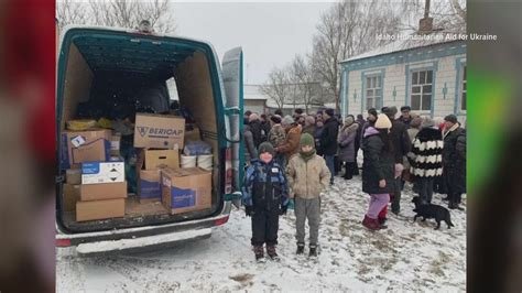 A van loaded with donated supplies beside residents gathered outdoors in winter in Ukraine