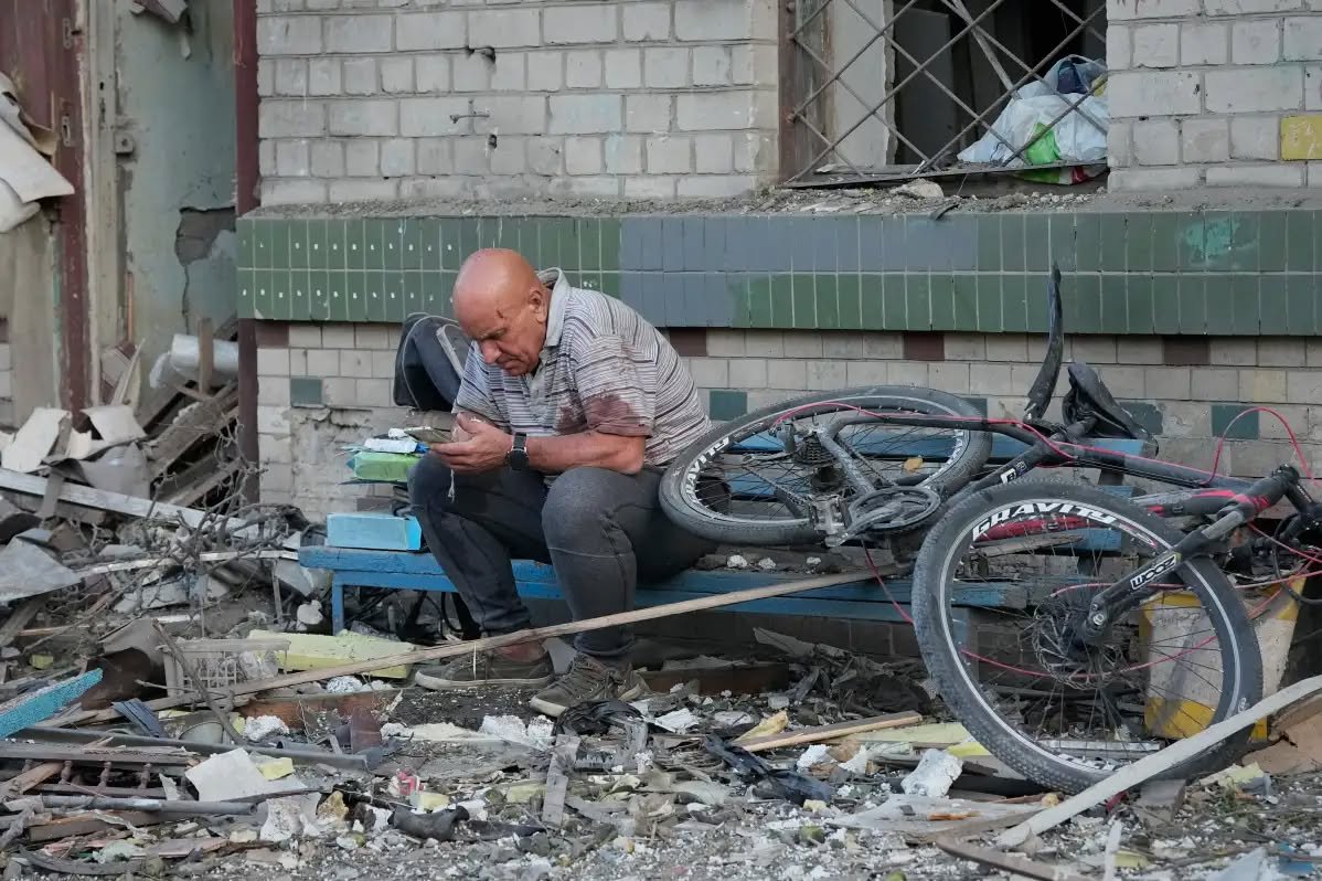 An older man sits among rubble outside a damaged building in Ukraine.